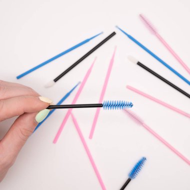 Kirpik uzatma araçlarındaki düz yüzeyin üst görünümü. Kadın eli tarama için renkli fırçalar tutuyor..