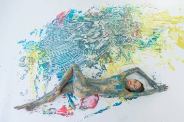 Çıplak bir kadının boya spreyindeki en iyi görüntüsü. Giysisiz bir kız, beyaz bir zeminde, renkli noktalarda yatıyor. Orijinal vücut resmi.