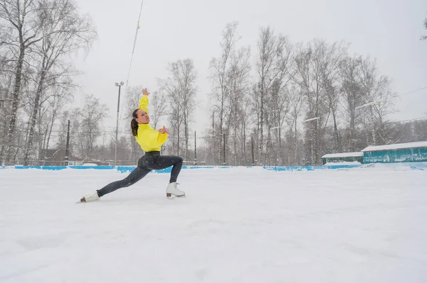 Um jovem patinador de gelo está treinando em uma pista de gelo ao ar livre em dezembro. Uma mulher entra para esportes de inverno. — Fotografia de Stock