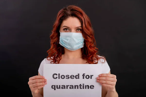 Red-haired woman in a medical mask holds a poster. Closed for quarantine. Epidemias of the coronavirus. Pandemic from China. Fear in the eyes.