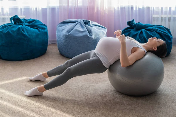 Hermosa mujer europea haciendo ejercicios de embarazo. La madre embarazada está haciendo ejercicios con una espada de fitness. Yoga para embarazadas . —  Fotos de Stock