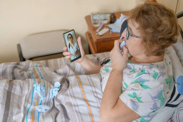 한연로 한 여성 이 코로나 바이러스에 걸려 현재 격리중이다. 한 연금 생활자는 침대에 누워 있으면서 바이러스성 질환에 대해 인터넷으로 의사와 상담 한다. — 스톡 사진