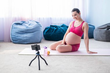 Hamile kadınlar için online dersler. Avrupalı bir kadın telefonda video fitness dersi veriyor. Bir mucize bekliyorum. Bekleyen anneler için yoga..