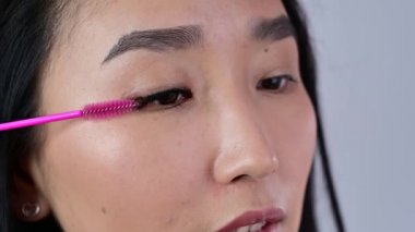 Uzatılmış kirpiklerini fırçayla fırçalayan Asyalı. Göz kapağı makyajlı, eli kulağında bir kadın. Güzellik endüstrisi. Kapat..