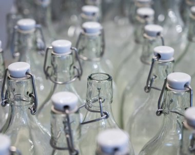 Bir şişenin boynuna yakın çekim. Tezgahtaki plastik kapaklı boş şişe grupları..