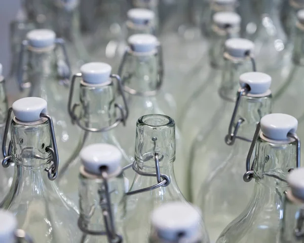 Bir şişenin boynuna yakın çekim. Tezgahtaki plastik kapaklı boş şişe grupları..