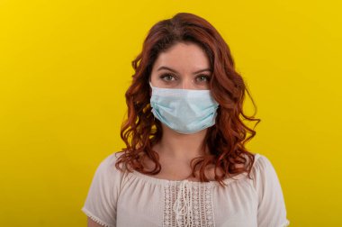 Tıbbi maskeli ürkek bir kadın. Antimikrobiyal solunum cihazında sarı arka planda kızıl saçlı bir kız..