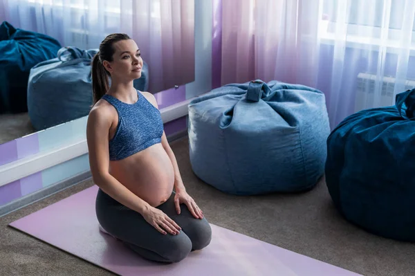 Een zwangere Europese vrouw doet alleen pilates. Verwachte moeder in het laatste trimester oefent yoga. Het meisje is 9 maanden uitgerekt.. — Stockfoto