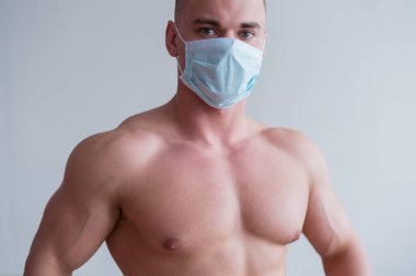 Göğüs kası kaslı, tıbbi maskeli bir erkek vücut geliştirici. Adam karantinaya spor için giriyor. Solunum koruması.