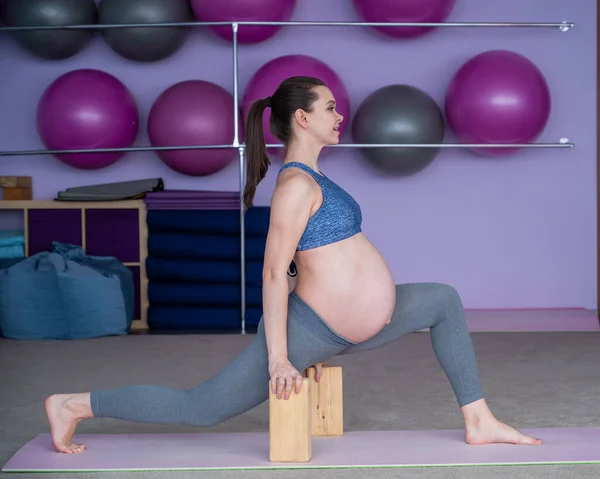 Zwanger flexibele Europese vrouw is bezig met fitness. De aanstaande moeder in het laatste trimester van de zwangerschap beoefent yoga met behulp van yoga blokken. — Stockfoto
