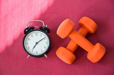 Pembe yoga minderinde iki turuncu tünel ve bir çalar saat. Evde ekipmanlarla spor yapma zamanı. Karantina spor disiplini