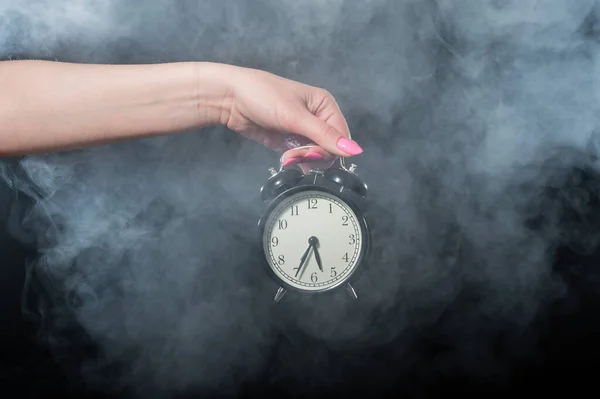 Una mujer sostiene un despertador en un estudio lleno de humo. Niebla blanca envolvió un reloj mecánico retro redondo . —  Fotos de Stock