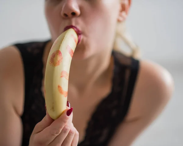 Eine Blondine in schwarzen Spitzenunterwäsche saugt und leckt erotisch eine Banane. Unerkennbare Frau mit sinnlichem Rot imitiert orales Vergnügen. — Stockfoto