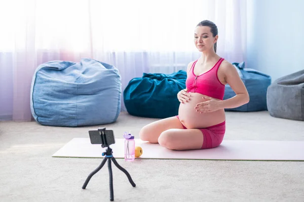 Online lekce pro těhotné ženy. Evropanka natočí video lekci fitness do telefonu. Čekám na zázrak. Jóga pro nastávající matky. — Stock fotografie