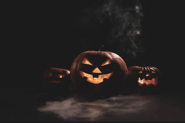 Halloween card. jack o lantern with candles glow on a black background. A row of creepy pumpkins with carved grimaces smokes in the dark. — Stock Photo, Image