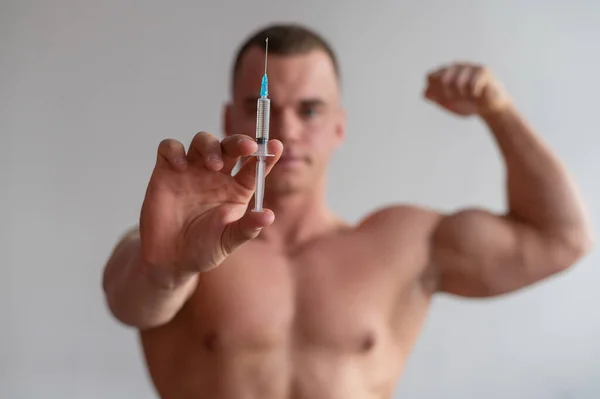 Culturiste masculin attrayant avec un torse nu tient une seringue de drogue. L'athlète se met une injection d'hormone de croissance . — Photo