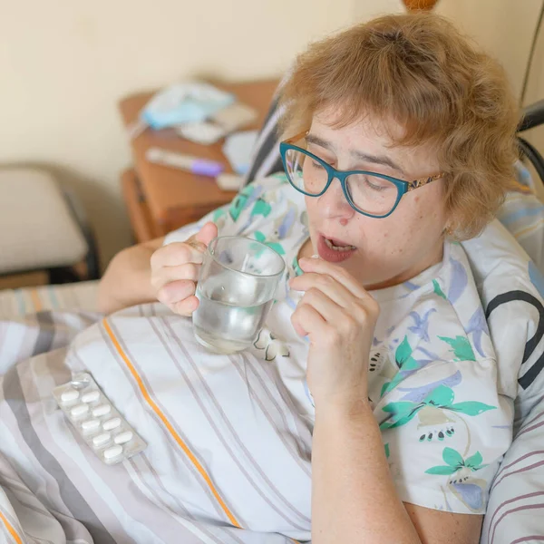 한연로 한 여자가 코로나 바이러스에 걸려 격리중에 있습니다. 연금 생활자는 침대에 누워 바이러스 성 호흡기 질환을 치료하기 위해 약물을 마신다. — 스톡 사진