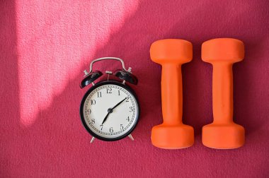 Pembe yoga minderinde iki turuncu tünel ve bir çalar saat. Evde ekipmanlarla spor yapma zamanı. Karantina spor disiplini