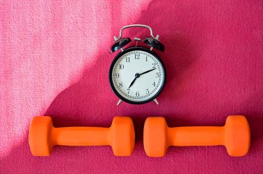 Pembe yoga minderinde iki turuncu tünel ve bir çalar saat. Evde ekipmanlarla spor yapma zamanı. Karantina spor disiplini