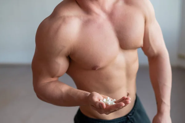 Body builder sans visage boit des capsules d'hormone de croissance. Un gros plan d'un homme musclé avec un torse nu contient une poignée de vitamines et de suppléments de fitness . — Photo