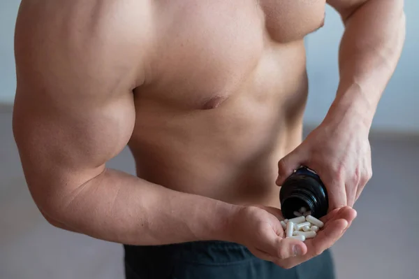 Body builder sans visage boit des capsules d'hormone de croissance. Un gros torse musculaire masculin verse une poignée de vitamines et de suppléments sportifs dans un bocal . — Photo