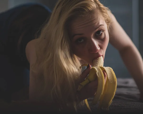 En blondin i svarta spets underkläder förföriskt suger och slickar en banan. Kvinna med sensuell röd imiterar oral njutning. — Stockfoto