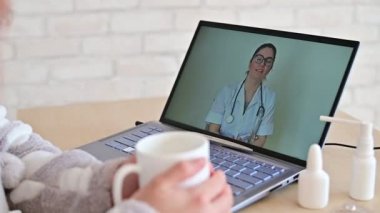 Bir kadın hastalık izninde. Hasta çevrimiçi bir doktora danışıyor. Bilgisayardaki doktorla görüntülü konuşma. Terapist hastalığın tedavisi için tavsiyeler verir..