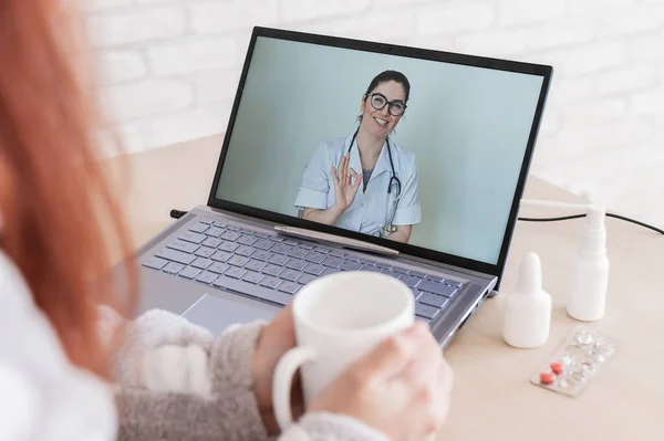 Una mujer está de baja por enfermedad. El paciente consulta a un médico en línea. Video chat con el médico en el portátil. El terapeuta da consejos para tratar la enfermedad . — Foto de Stock