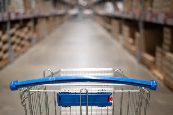 Carrinho de compras vazio em um armazém de loja de móveis. Supermercado shopping cesta corredor com caixa prateleira abstrato borrão desfocado fundo — Fotografia de Stock