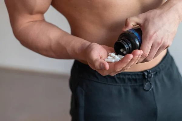 Tanınmayan vücut geliştiren adam vitamin kapsülleri içiyor. Büyük bir erkek kaslı gövde kavanozdan bir avuç dolusu spor malzemesi döker.. — Stok fotoğraf