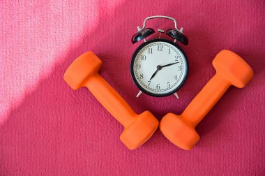 Pembe yoga minderinde iki turuncu tünel ve bir çalar saat. Kendi kendini izole etme zamanı geldi. Evde ekipmanlı spor.