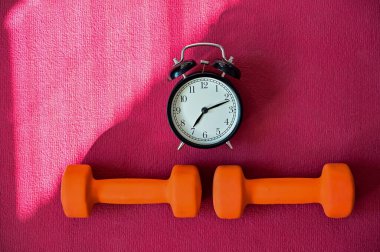 Pembe yoga minderinde iki turuncu tünel ve bir çalar saat. Evde ekipmanlarla spor yapma zamanı. Karantina spor disiplini