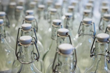 Bir şişenin boynuna yakın çekim. Tezgahtaki plastik kapaklı boş şişe grupları..