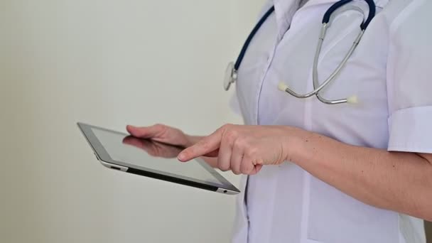 Nierozpoznawalna lekarka w mundurze używa tabletu. Pracownik medyczny kontaktuje się z pacjentami na urządzeniu. Przycięte. — Wideo stockowe