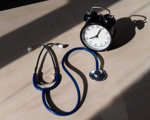 Estetoscópio e despertador em uma mesa de madeira à luz do sol. Uma ferramenta para medir a pressão arterial. Cardiologista de mesa . — Fotografia de Stock