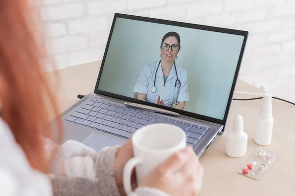 Una mujer con un resfriado está de baja por enfermedad y está mirando una consulta de vídeo portátil frendly médico. Un paciente en una cita remota. Reunión en línea . — Foto de Stock