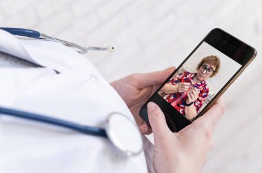 Tanımlanamayan kadın doktor, akıllı bir telefonla online danışmanlık yapıyor. Yaşlı bir kadında koronavirüs var. Cep telefonundan terapiste görüntülü arama. Karantina.