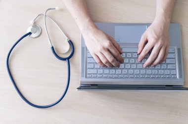 Klavyedeki ellerin üst görüntüsü. Masada dizüstü bilgisayarda yazan kadın doktor. Hemşire hasta elektronik kartını doldurur..