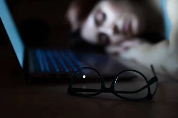 Fáradt nő, aki a munkahelyén alszik a laptop mellett. A lány elszunyókált egy távoli melóba. A túlhajszolt diák elaludt az asztalon. Szemüveg az előtérben. — Stock Fotó