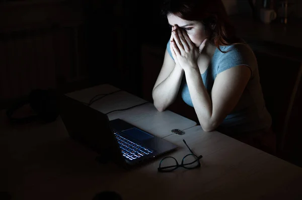 Femme fait des heures supplémentaires. Un étudiant étudiant sur un ordinateur portable la nuit dans le noir. La fille est inquiète des problèmes au travail et tient ses mains sur son visage . — Photo