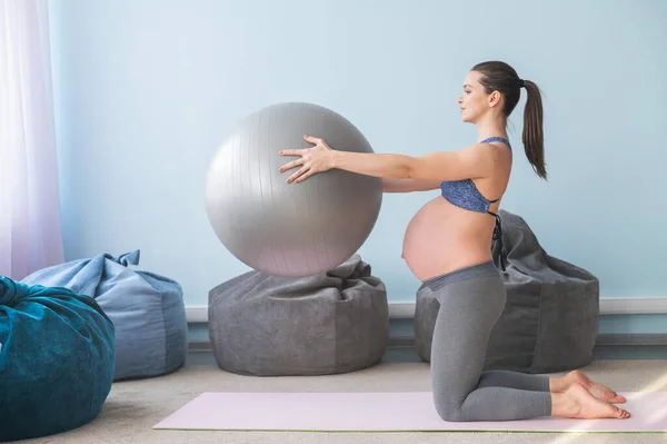 Zwangere Europese vrouw voert oefeningen met fitness bal. Verwachte moeder doet yoga in het derde trimester. Meisje in de klas ter voorbereiding op de bevalling. — Stockfoto