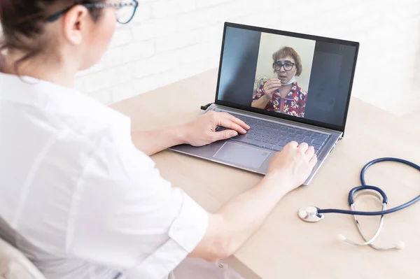 An elderly woman with the flu for an online consultation with a doctor. Female practitioner makes a video call with a patient on a laptop. A pensioner on the remote doctors office.