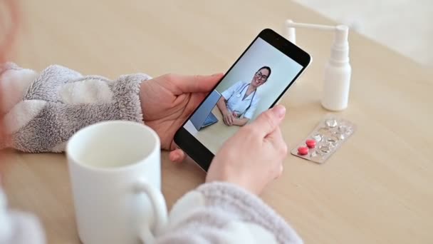 Oigenkännlig kvinna på online konsultation med en läkare på en mobiltelefon. Flickan är sjuk och pratar med läkaren på ett videosamtal hemifrån. Närbild av skärmen. — Stockvideo
