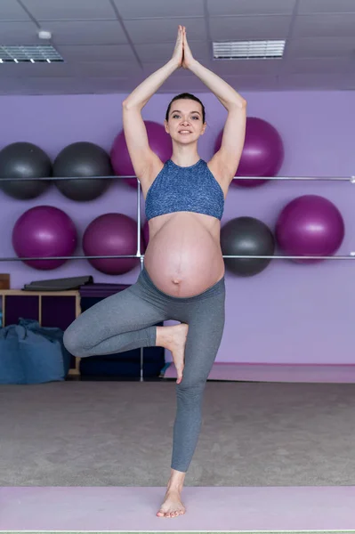 Těhotná žena ve třídě jógy. Budoucí matka s nahým bříškem se věnuje fitness. Pozice stromu. Čekající. — Stock fotografie