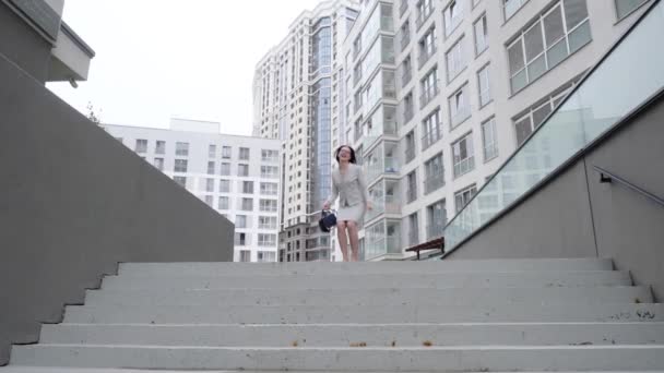 Exitosa mujer de negocios bailando y saltando de alegría en la calle. Hermosa chica en un traje de negocios se regocija en las escaleras. Movimiento lento . — Vídeos de Stock