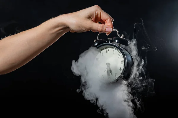 Una mujer sostiene un despertador en un estudio lleno de humo. Niebla blanca envolvió un reloj mecánico retro redondo . —  Fotos de Stock