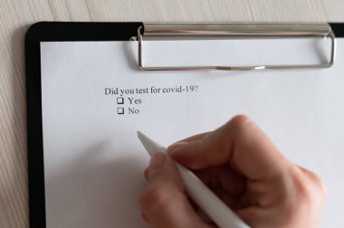 Tanımlanamayan bir kadın ankete bir daw koyar. Bir kadın eli yakın çekimde bir covid-19 sorusuna cevap veriyor. bir onay kutusunda işaretleme