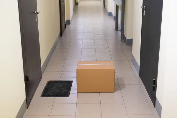 Ανέπαφη πόρτα παράδοση έννοια. Χάρτινο κουτί με ηλεκτρονική αγορά από την μπροστινή πόρτα στην άδεια αίθουσα μιας πολυκατοικίας. — Φωτογραφία Αρχείου