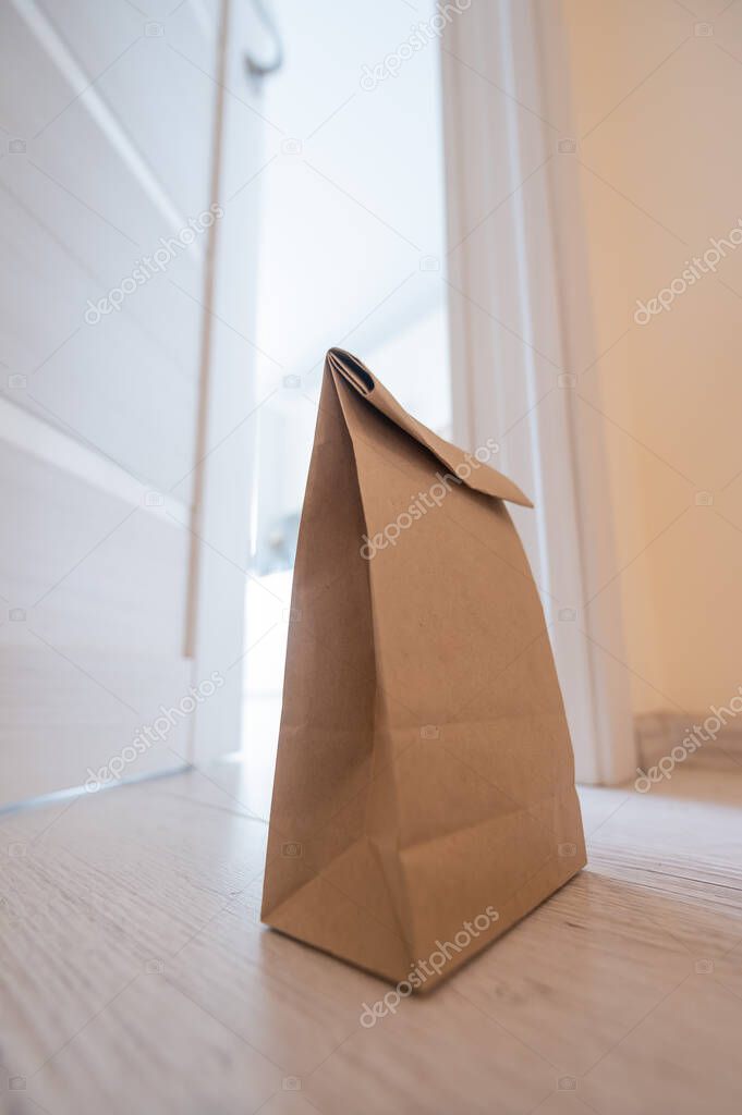 The concept of contactless delivery during the quarantine period. Kraft paper bag with online purchase at the open entrance door in case of danger of the spread of coronavirus.