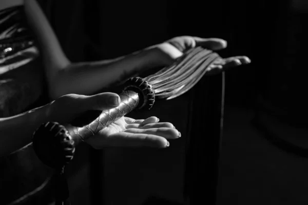 Närbild Svart läderfrans i kvinnliga händer. Monokrom beskärda foto av bdsms leksaker. En kvinna står i mörkret och håller en piska i handflatorna. — Stockfoto